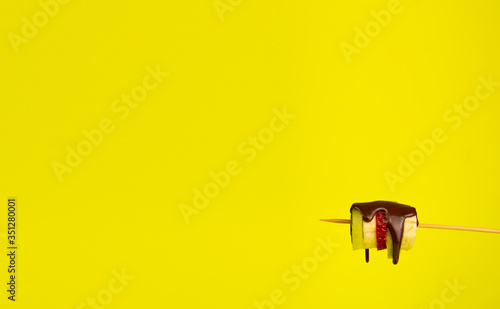 Fresh fruit drenched in liquid chocolate on a stick. Yellow background and place for an inscription