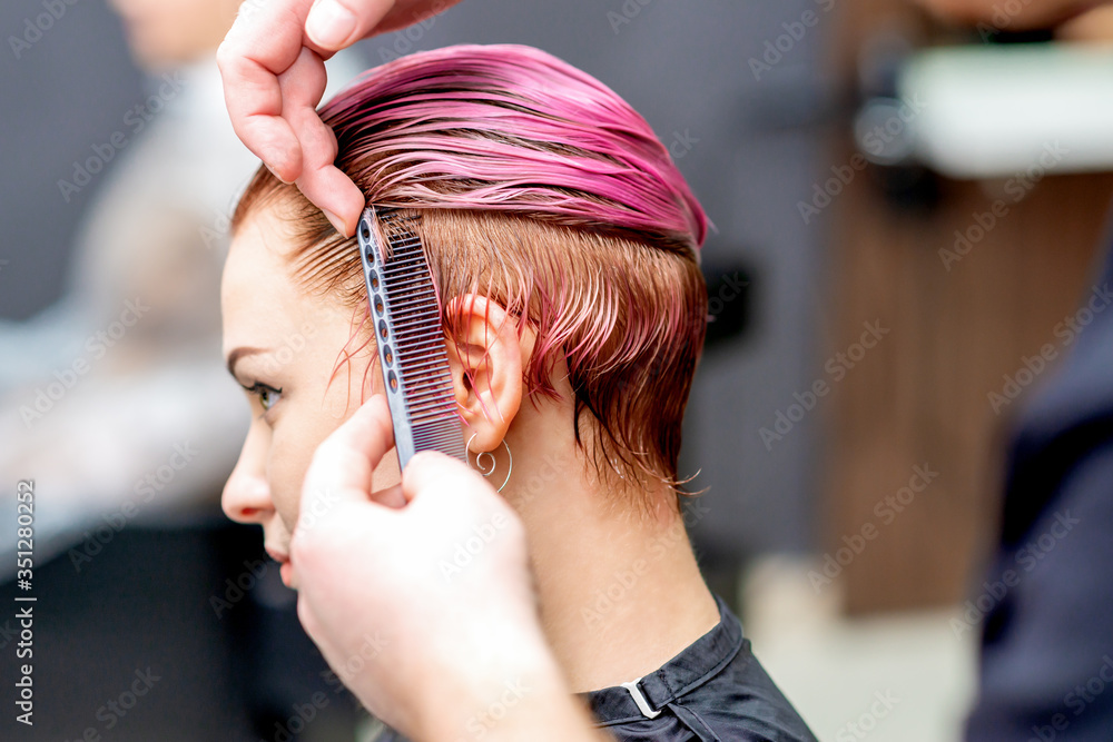 Naklejka premium Hands of hairdresser are combing woman hair in salon, close up.