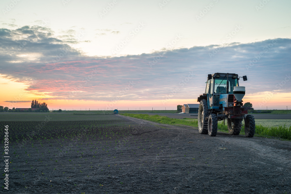 Fototapeta premium Tractor is parked on an agricultural field with beautiful colored clouds in the background