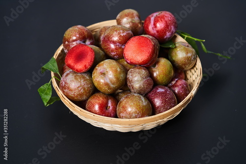 Fresh plums in a woven bamboo basket against a black background