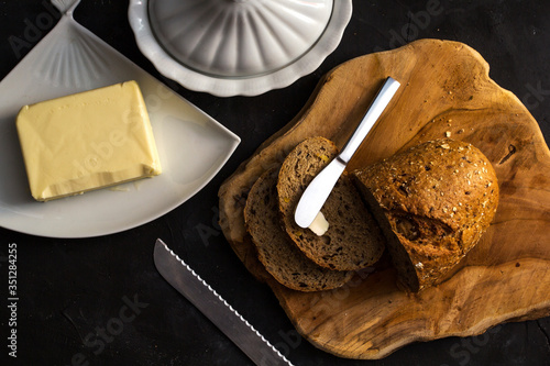 Loaf of bread with butter and knife. Dark background. top view