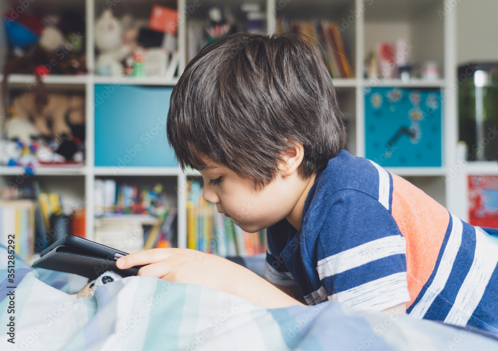 Kid self isolation using tablet for his homework,Childlying in bed using digital tablet searching information on internet,Home schooling,Social Distance,E-learning online education Kid self isolation using tablet for his homework,Childlying in bed using digital tablet searching information on internet,Home schooling,Social Distance,E-learning online education