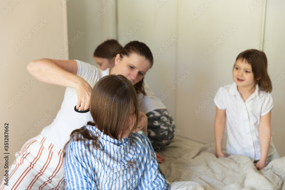 Caucasian mom cuts her kid at home, siblings look Caucasian mom cuts her kid at home, siblings look