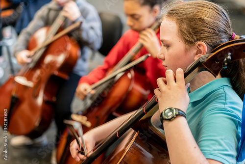 Teenage girls and boy playing cellos in classroom