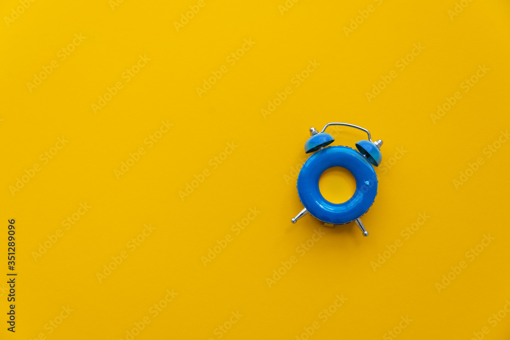 Vacation time. Blue alarm clock as swimming ring form on yellow background. Top view. Copy space Vacation time. Blue alarm clock as swimming ring form on yellow background. Top view. Copy space