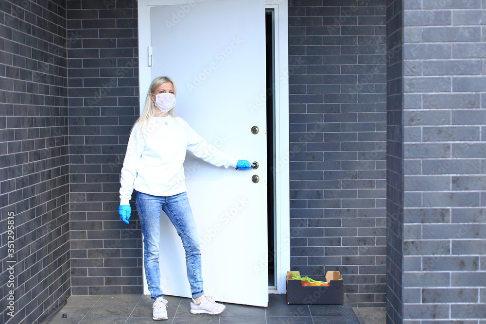 A young girl is standing on the porch in a respiratory mask and gloves.