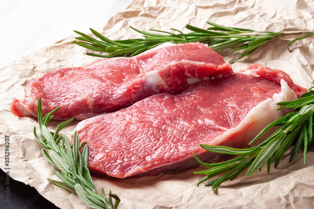 Raw meat . Two slices of fresh raw meat and a branch of rosemary on paper. Preparing meat for a barbecue.