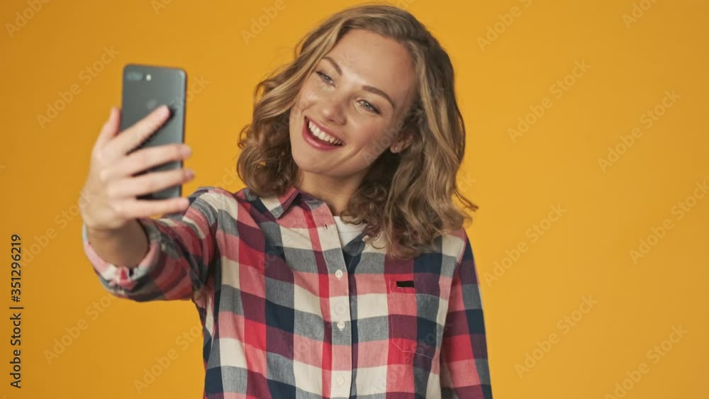Young happy girl isolated over yellow wall background take a selfie by mobile phone Young happy girl isolated over yellow wall background take a selfie by mobile phone