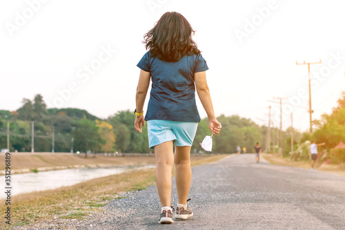 Sportive woman take off protective mask while jogging for easier breathing on road beside irrigation canal due to the corona virus (Covid-19) outbreak. New normal lifestyle concept.