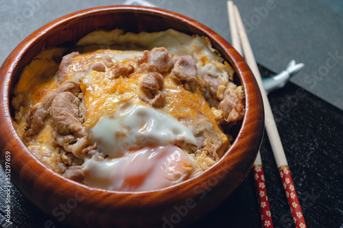 Baked Pork Rice with Eggs in a Wooden Bowl, Kitchen Tableware, Top View Green Wood Background with Natural Light by Morning Window, Japanese style food, Selective focus.