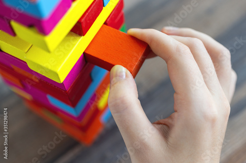 Close up of a hand pulling a colorful  jenga block from a big pile. Fun board games concept photo
