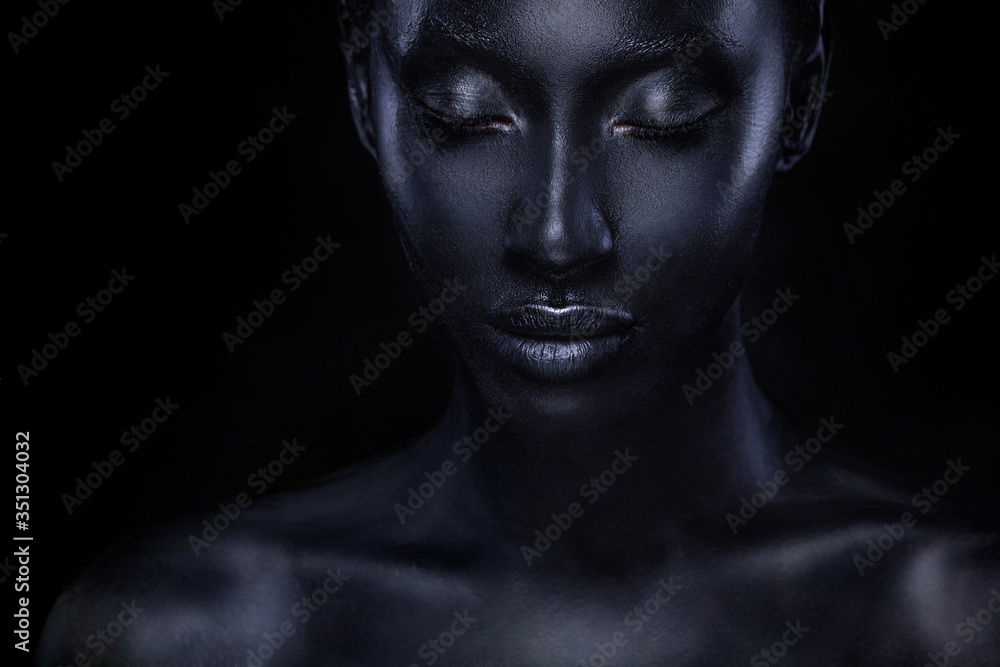 Woman with black body paint. Cheerful young african girl with bodypaint. An amazing model with art makeup. Closeup face.