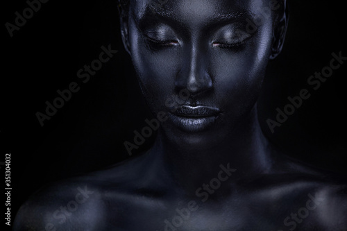 Woman with black body paint. Cheerful young african girl with bodypaint. An amazing model with art makeup. Closeup face. photo