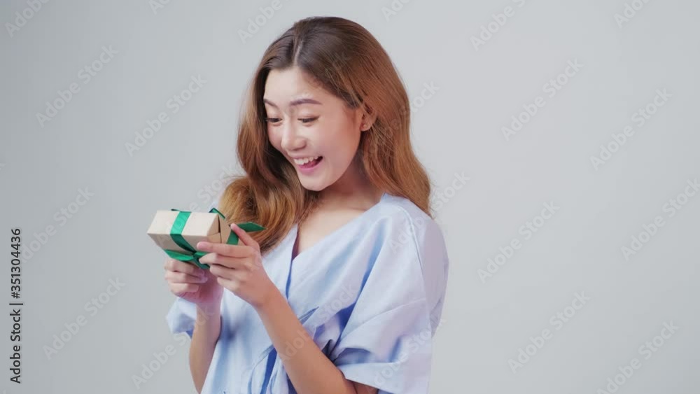 Asia girl wearing a patient gown having big smile surprise with excitement when getting the present, gift box when recovery, the concept of trust in insurance, compensation, insurance advertisement. Asia girl wearing a patient gown having big smile surprise with excitement when getting the present, gift box when recovery, the concept of trust in insurance, compensation, insurance advertisement.