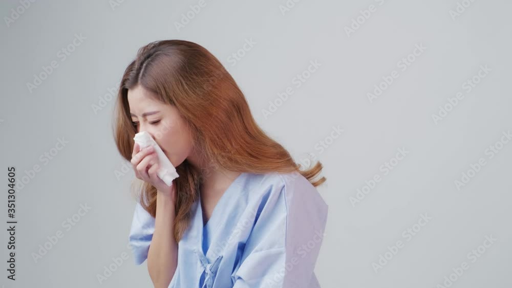 Unhealthy Asia girl wearing patient gown sneezing feeling sick suffer from allergy or flu symptoms, spreading germ and virus during Coronavirus pandemic, concept of healthcare and insurance, illness. Unhealthy Asia girl wearing patient gown sneezing feeling sick suffer from allergy or flu symptoms, spreading germ and virus during Coronavirus pandemic, concept of healthcare and insurance, illness.