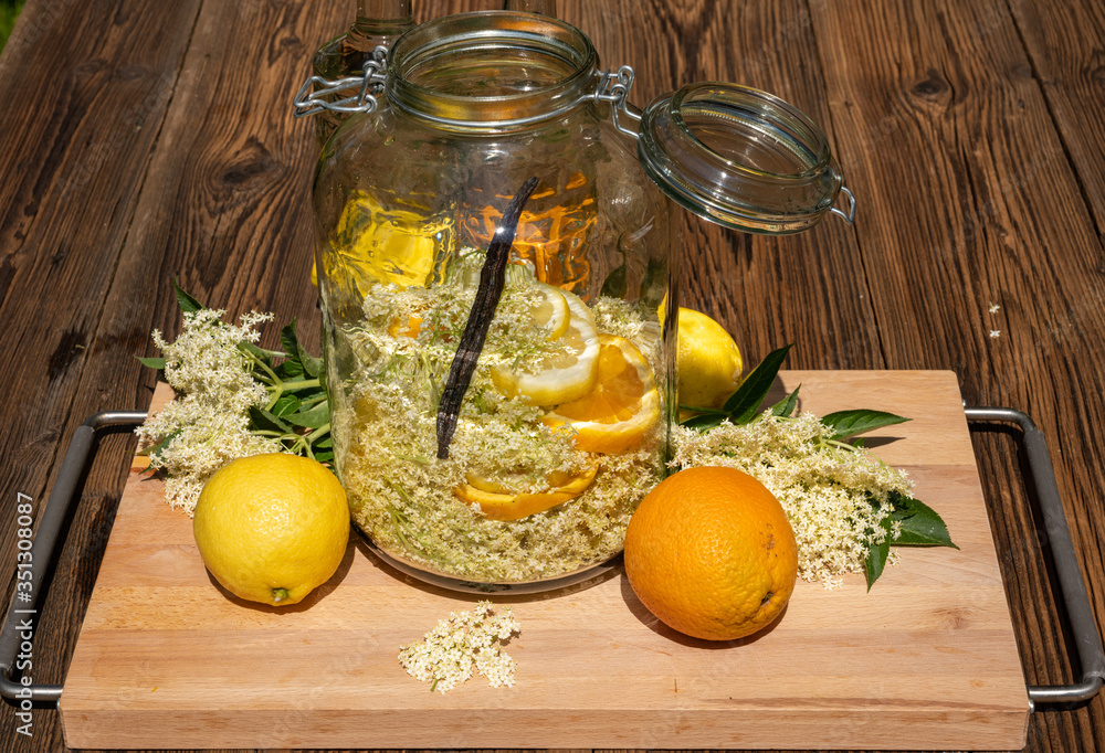 In the large preserving jar on the cutting board are the fresh elderflowers, oranges and lemon slices and the vanilla pod for the elderflower liqueur In the large preserving jar on the cutting board are the fresh elderflowers, oranges and lemon slices and the vanilla pod for the elderflower liqueur
