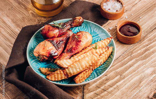Chicken drumsticks with french fries on blue plate on rustic wooden table.