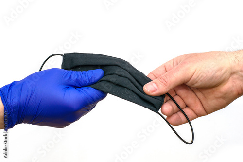 hand in a blue medical protective glove hands over a black medical mask to an unprotected hand on a white background