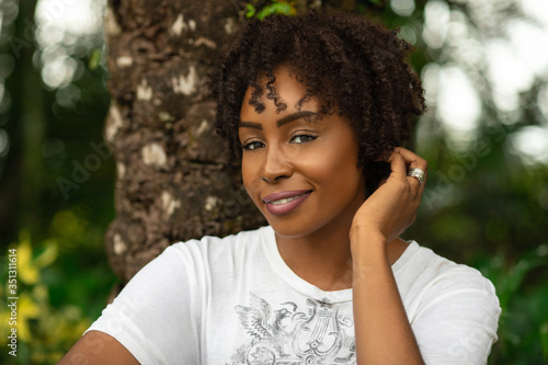 Natural portrait of an attractive black female with medium sized natural curly black & brown hair & beautiful eye makeup posing by herself underneath a palm tree.