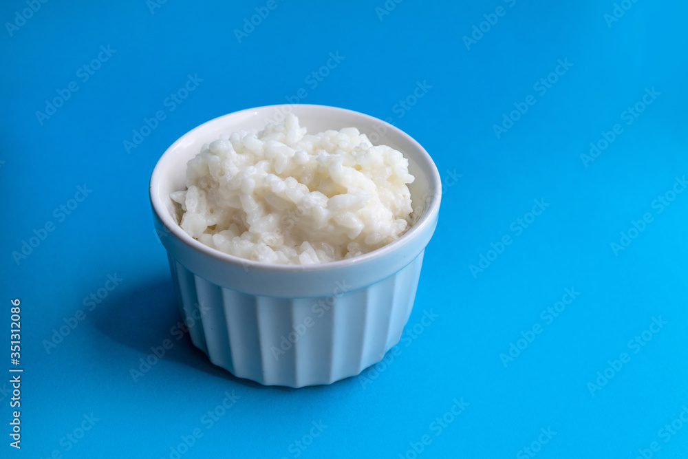 Tasty rice porridge in a white bowl on blue background. Proper healthy eating breakfast concept. Tasty rice porridge in a white bowl on blue background. Proper healthy eating breakfast concept.