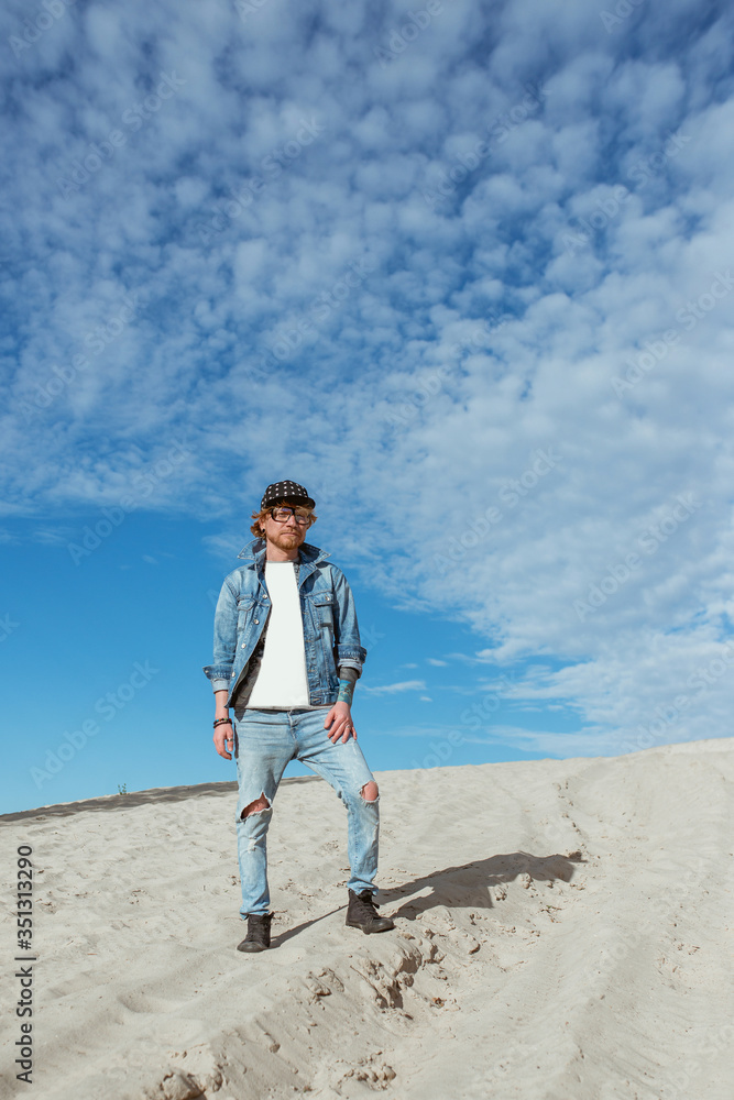 portrait of stylish man in jeans clothes and hat in glasses in the desert. Male, style, fashion, nature concept portrait of stylish man in jeans clothes and hat in glasses in the desert. Male, style, fashion, nature concept