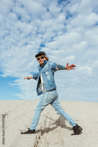 portrait of stylish funny man in jeans clothes and hat in glasses jumping in the desert. Male, style, fashion, nature concept