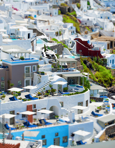 Top view from above of Santorini villas. Panorama of small houses with blue water swimming pool on white terrace, blur background © GeorgeTsamakdas