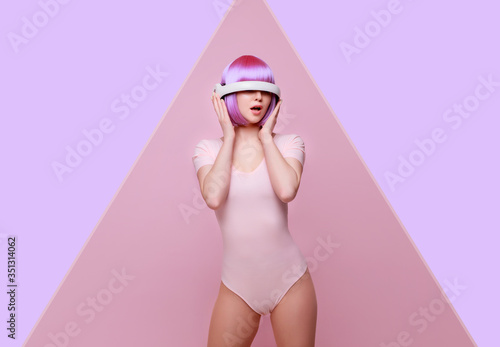 Beautiful young woman with purple hair over bright trendy pink background. Girl in glasses of virtual reality. Augmented reality game, future technology, AI concept. VR.