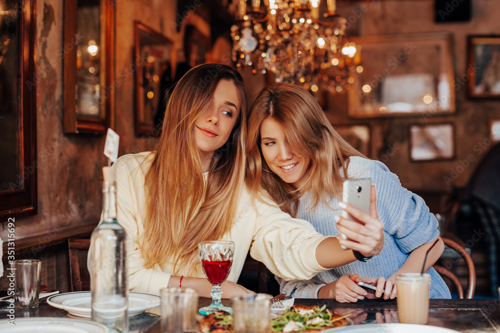 Fototapeta premium funny meeting of two friends after quarantine in a restaurant, girls exchange good news and take selfie on the phone. selfie time 