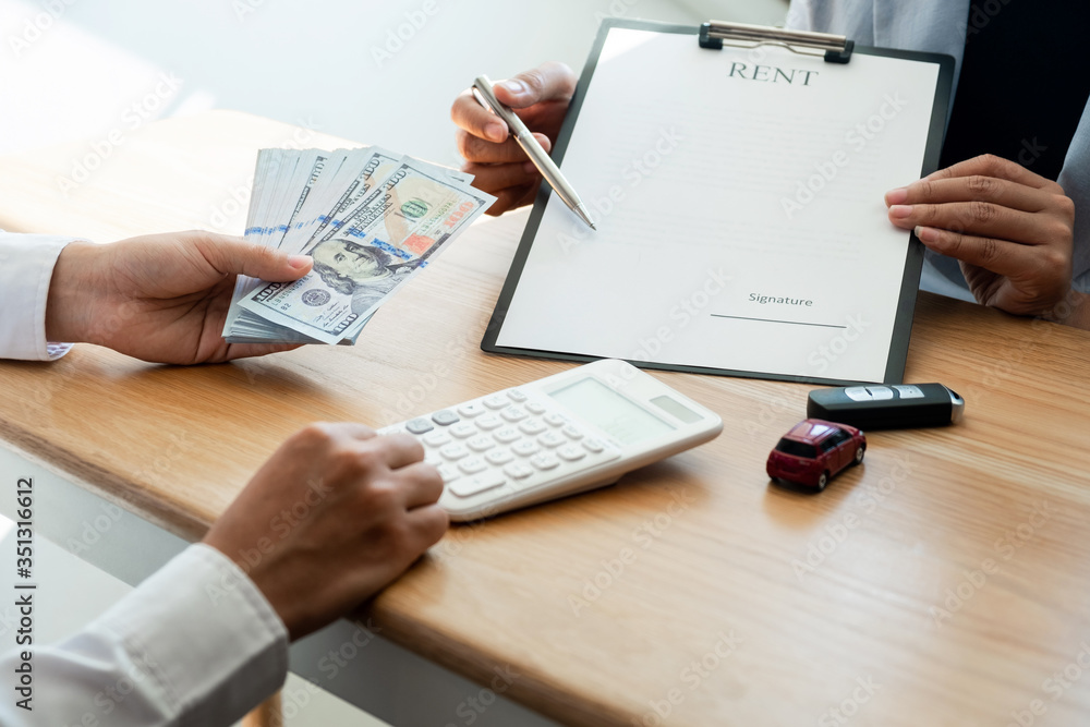 Customer is signing the car rental agreement and getting a car key from dealer after signed in the office. Customer is signing the car rental agreement and getting a car key from dealer after signed in the office.