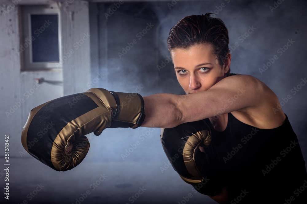 Closeup image of a female boxer punching with boxing gloves and looking at the camera
