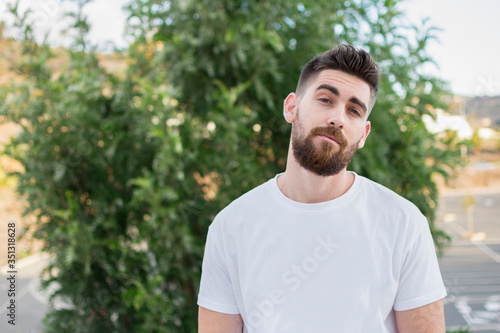 Handsome man with a beard and white t-shirt outdoors.