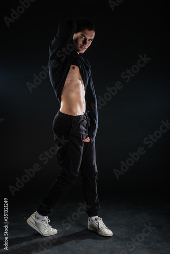 Sexy male model lifting his black blouse and showing his abs while posing in a studio on a black backgorund.