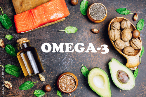 Animal and vegetable sources of omega-3 acids as salmon, avocado, linseed, nuts, almonds, chia seeds, spinach and olive oil on dark background. Top view. flat lay. Lettering - Omega 3