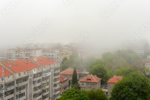 Residential lowrise houses and streets with green trees in dense fog at summer day. Thick fog came from the sea and covered the city. Climate and weather changes.