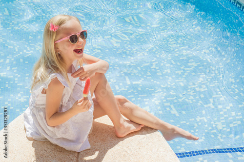 Summertime fun. Happy little girl eating ice cream near the pool
