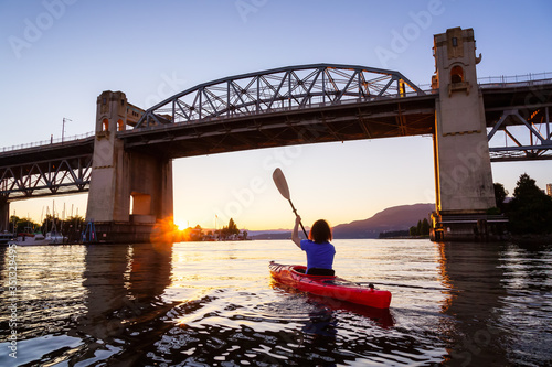 Girl Kayaking in a Modern City during a vibrant golden sunny sunset. Taken in False Creek, Downtown Vancouver, British Columbia, Canada. © edb3_16