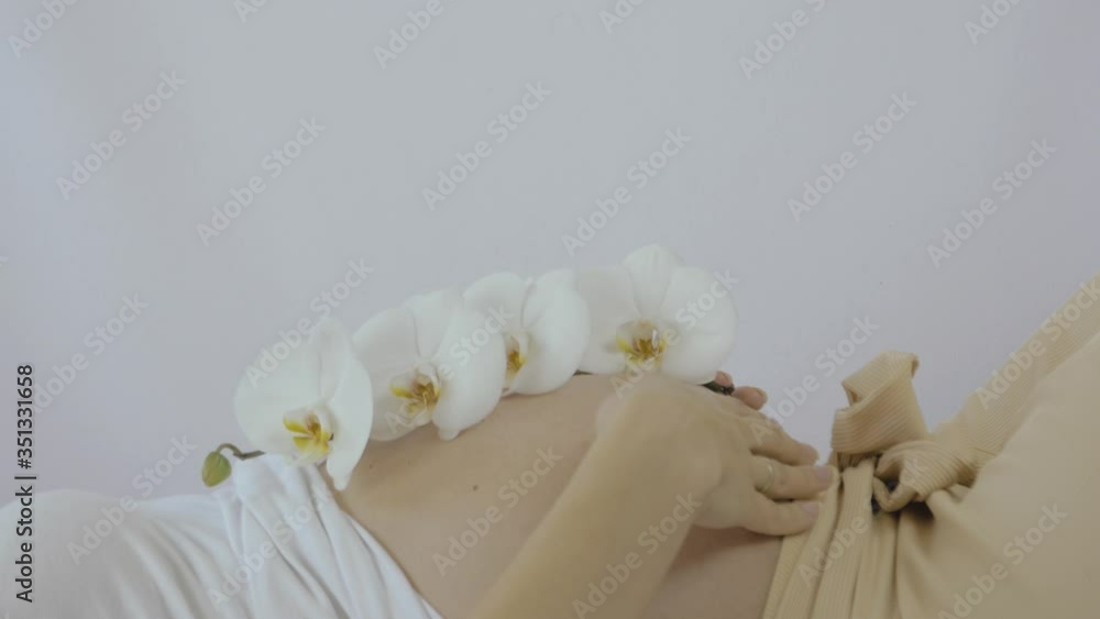 Pregnant woman practicing breathing prenatal exercises with beautiful flowers orchids on white background. Relaxation and delivery preparation mindfulness concepts. Sports concept. Pregnant woman practicing breathing prenatal exercises with beautiful flowers orchids on white background. Relaxation and delivery preparation mindfulness concepts. Sports concept.