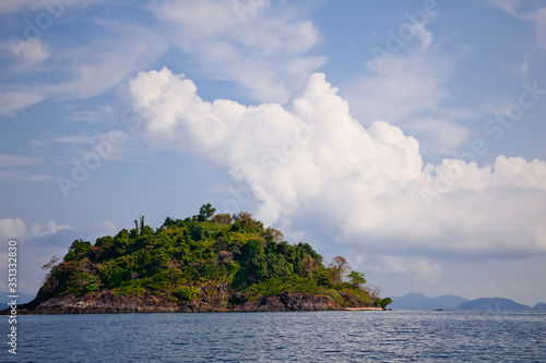 A small uninhabited green island in the ocean against a cloudy sky