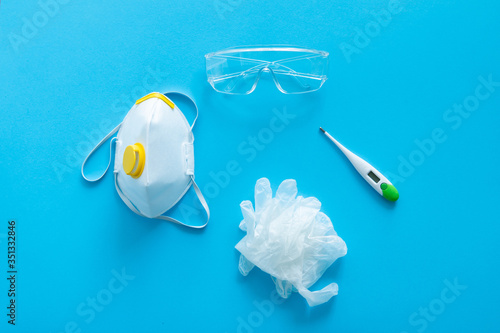 Respirator ffp, rubber gloves, thermometer and protective glasses lie on a blue background. Anti-virus protection kit against covid-19. Coronavirus pandemic 2019.