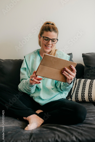 Happy beautiful woman watching videos or enjoying entertainment content on a tablet sitting on the sofa. home working