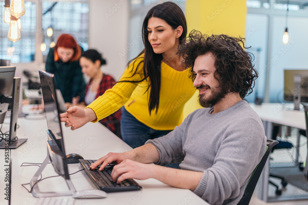 Obraz premium An attractive business girl standing next to a happy male colleague with clumsy hair and they are discussing new strategies in a modern office.