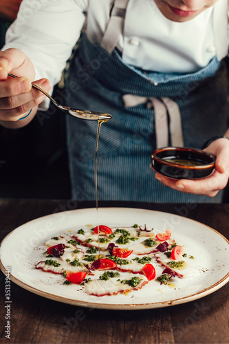 Chef preparing Octopus Carpaccio, pouring sauce on a plate, kitchen work. 