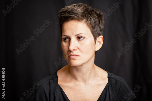 A serious and distracted woman with a short haircut and gray hair looks away. Loneliness. Close-up. Black background. © Анна Демидова