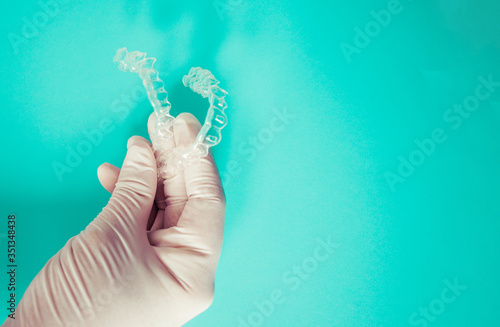 Doctor's hand teaches clear dental aligners on sky-blue background with copy space