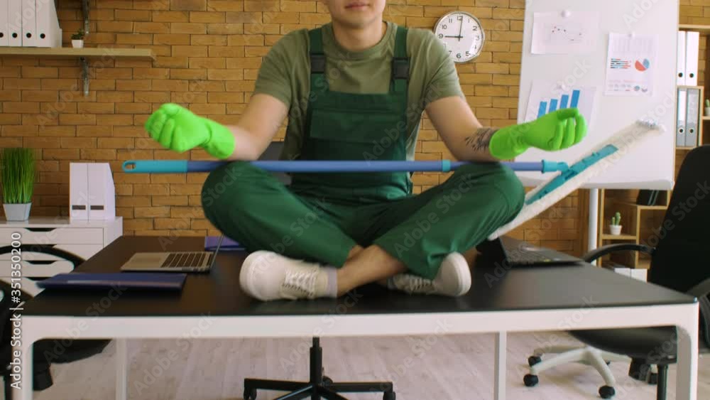 Male Asian janitor meditating while sitting on table in office Male Asian janitor meditating while sitting on table in office