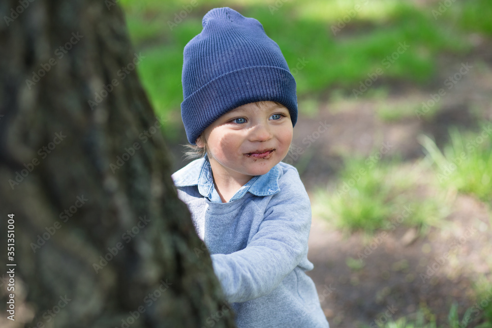 Smiling curly baby in a blue hat plays in the park Smiling curly baby in a blue hat plays in the park