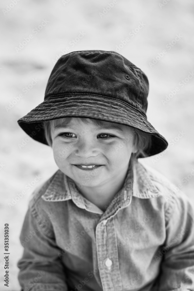 Smiling curly baby in a blue hat plays in the park