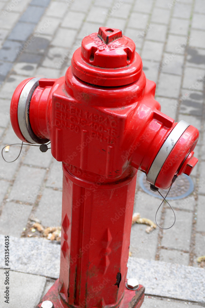A red fire hydrant against a tiled road in a European city during the day. fire safety