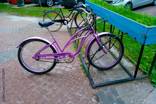 A beautiful lilac bike for women stands on a sidewalk paved with a decorative stand in the rain. Street parking for cycling in the city. Close-up.